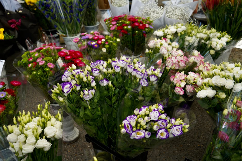 A variety of fresh flowers arranged in bouquets on a display table for flower delivery, featuring purple and white lisianthus, white and pink roses, and small red, pink, and purple chrysanthemums. The