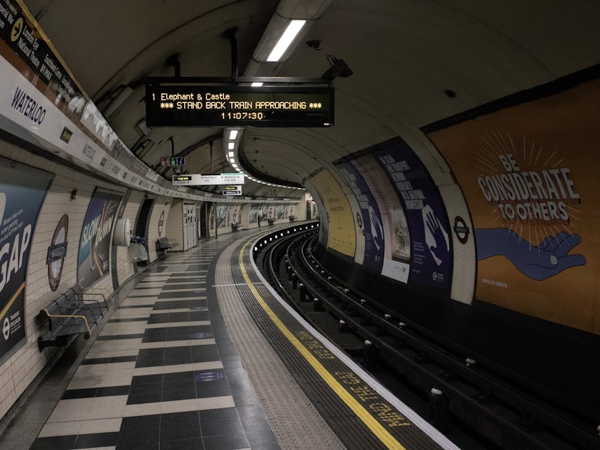 Empty platform of the London Underground at Elephant and Castle station, with a curved track disappearing into a dark tunnel. The platform features black and white checkered flooring, and a row of bla